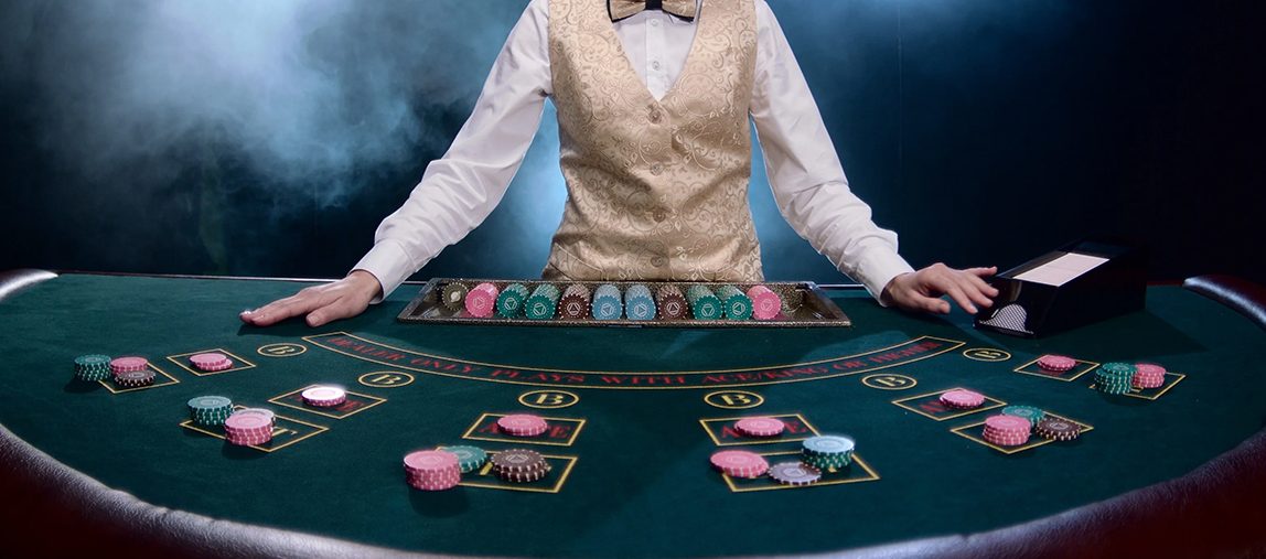De croupier in het casino aan de pokertafel legde de fiches neer en maakte zich klaar om kaarten uit te delen, tegen de achtergrond van neerdalende rook